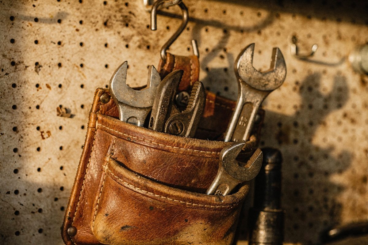 Worn leather tool belt with wrenches and a pipe cutter hanging on a workshop pegboard